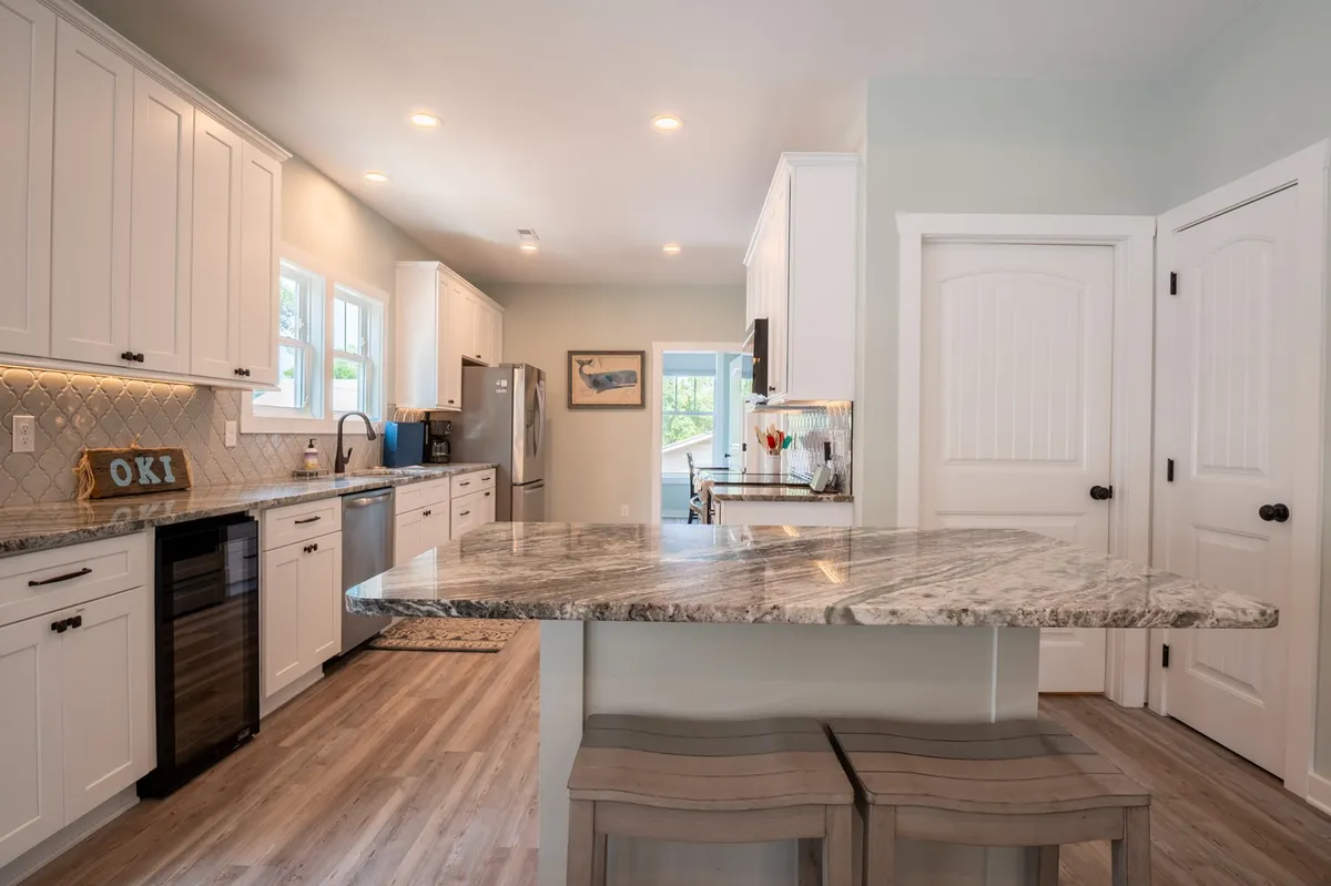 A beautifully designed kitchen with granite countertops, white cabinetry, stainless steel appliances, and a generous island with stools. The space is bright and welcoming, clearly set up for cooking and casual dining, with enough room for several people to gather and participate.