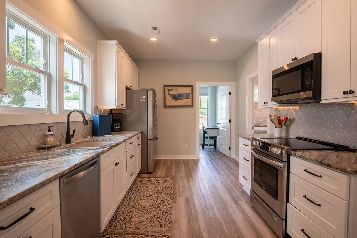 An open kitchen with granite countertops and stainless steel appliances, bathed in warm natural light. A window offers a glimpse of the outside, and the adjacent dining area is visible through a doorway, hinting at space for group gatherings after outdoor activities.