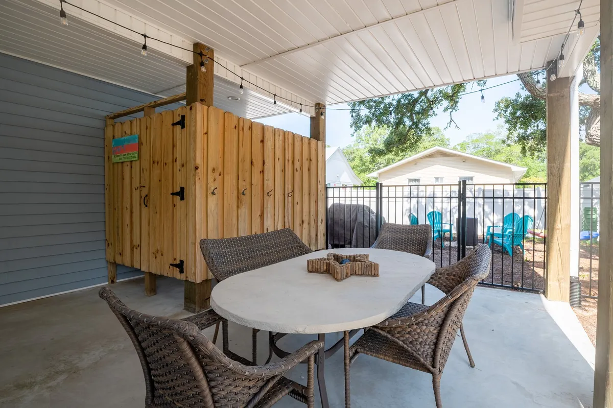 A view of the private, fully fenced outdoor area featuring a spacious dining table with wicker chairs, surrounded by a wooden privacy fence. The area is shaded, creating a comfortable space for al fresco meals and gatherings.