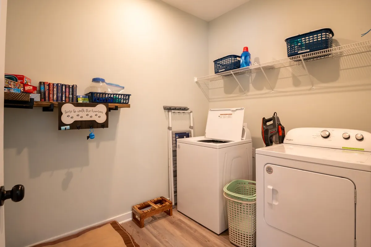 A practical laundry room equipped with a washing machine, drying machine, shelving unit, and laundry baskets. The space is organized and welcoming, perfect for handling sandy towels and clothes after a beach day.