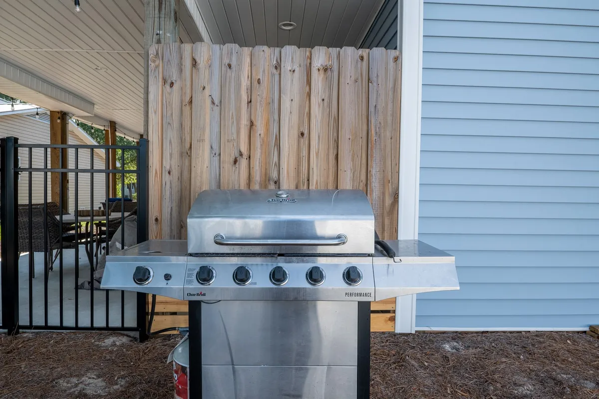 This exterior image highlights the backyard entertaining area, complete with a grill, wooden fence, and comfortable seating. The setup is inviting for barbecues and casual outdoor meals, with the fence reinforcing pet-friendly safety.