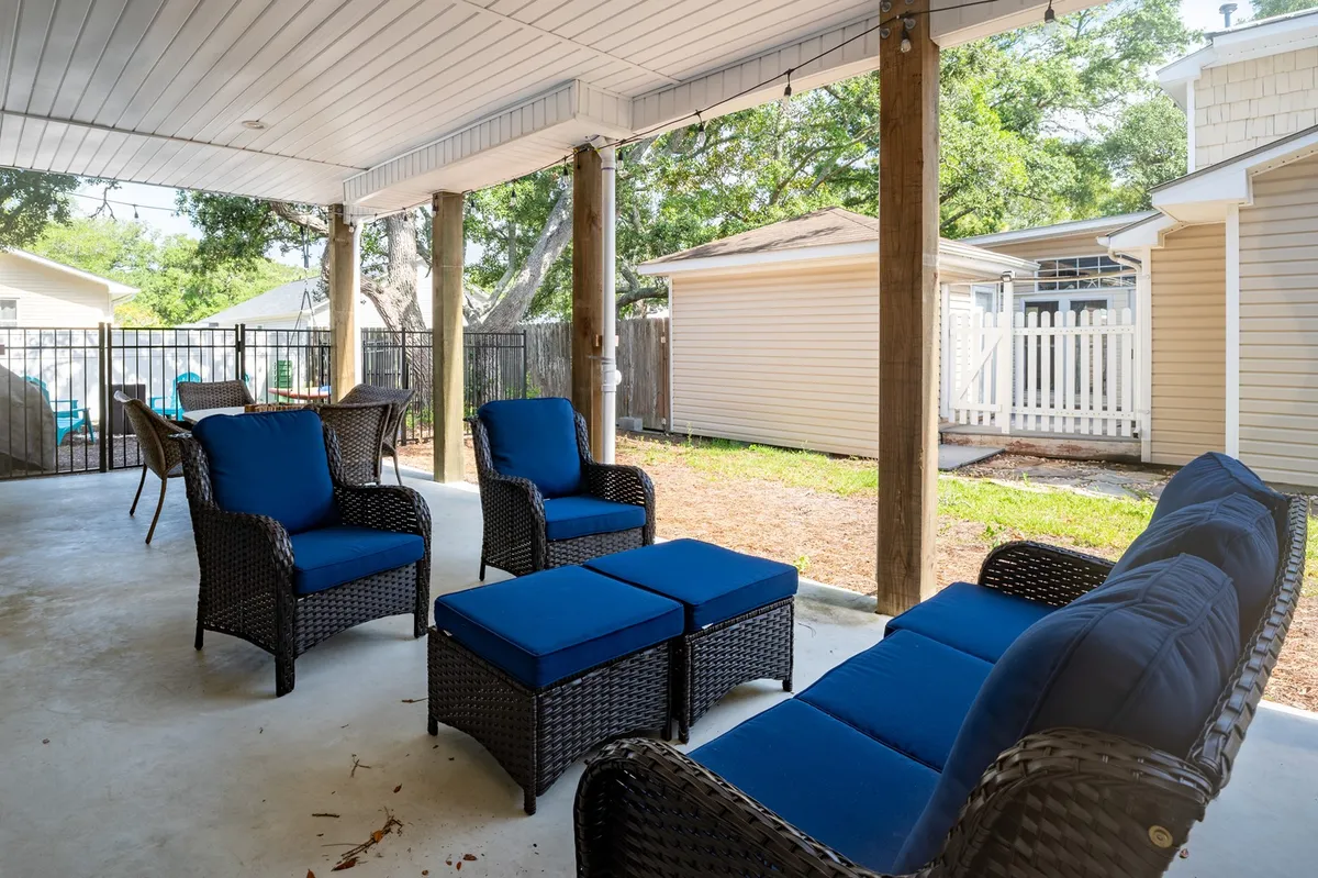 A cozy backyard lounge setup with wicker furniture and blue cushions, positioned to take in the open backyard view. The arrangement invites relaxing, socializing, or enjoying casual meals, and the space feels intimate yet open—a great spot for sunset gatherings or game nights.
