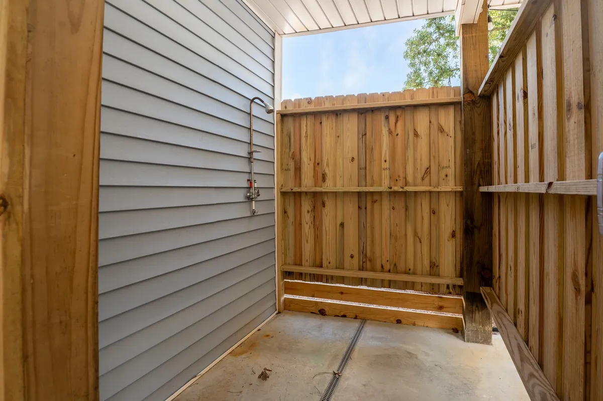 A stylish outdoor shower area bordered by a wooden privacy fence, with a contemporary showerhead set against a textured wall. The space offers privacy and a sense of connection with nature, ideal for rinsing off after beach days or outdoor activities.