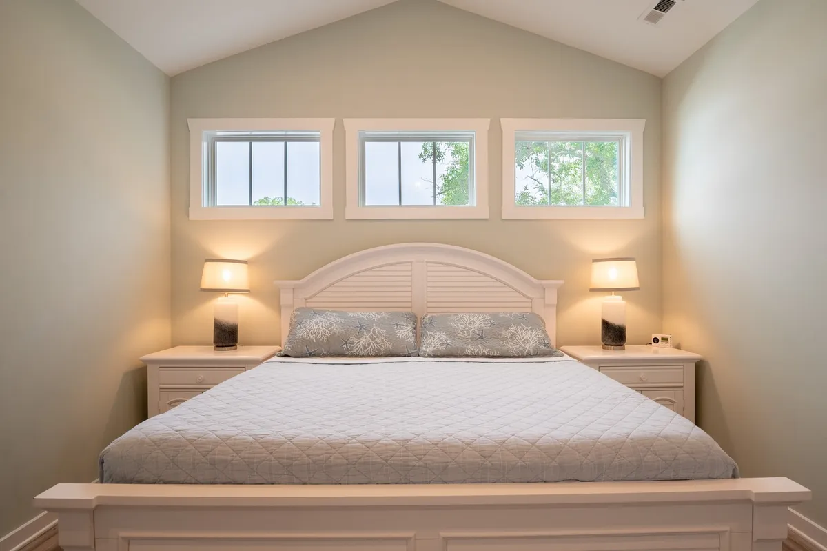 A serene bedroom with a neatly made bed, nightstands on either side, and windows that let in ample natural light. The soft color palette and uncluttered decor create a peaceful and restful ambiance, perfect for unwinding after a long day.