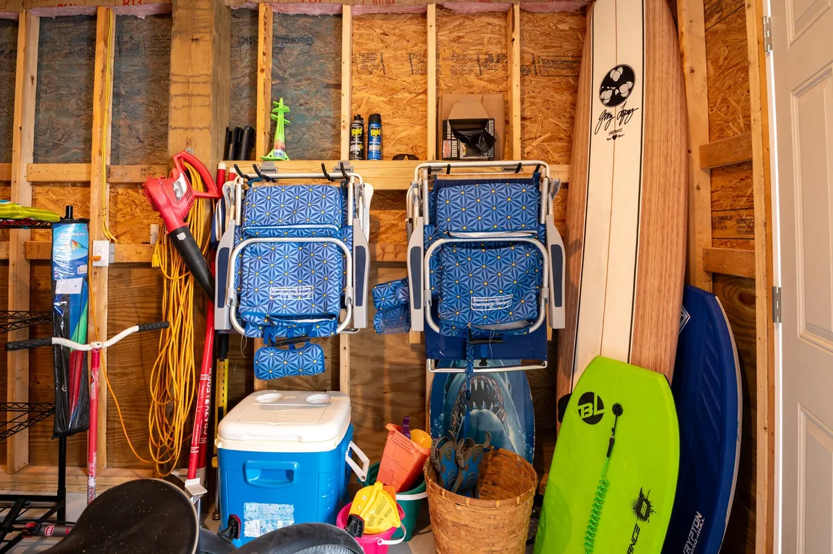 A playful and well-organized storage area featuring beach chairs, a surfboard, a cooler, beach toys, and open shelving. The space is clearly designed for easy access to items needed for family outings.